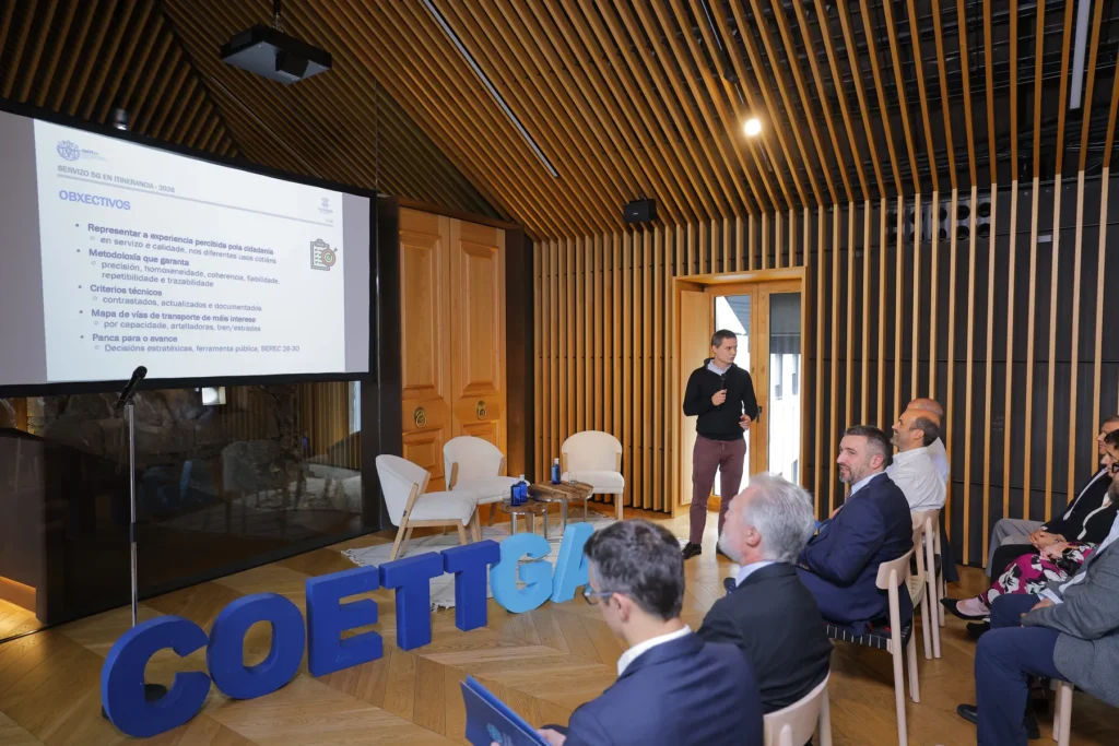 Ante asistentes atentos, un relator comenta a diapositiva de obxectivos xunto ás letras azuis COETTGA