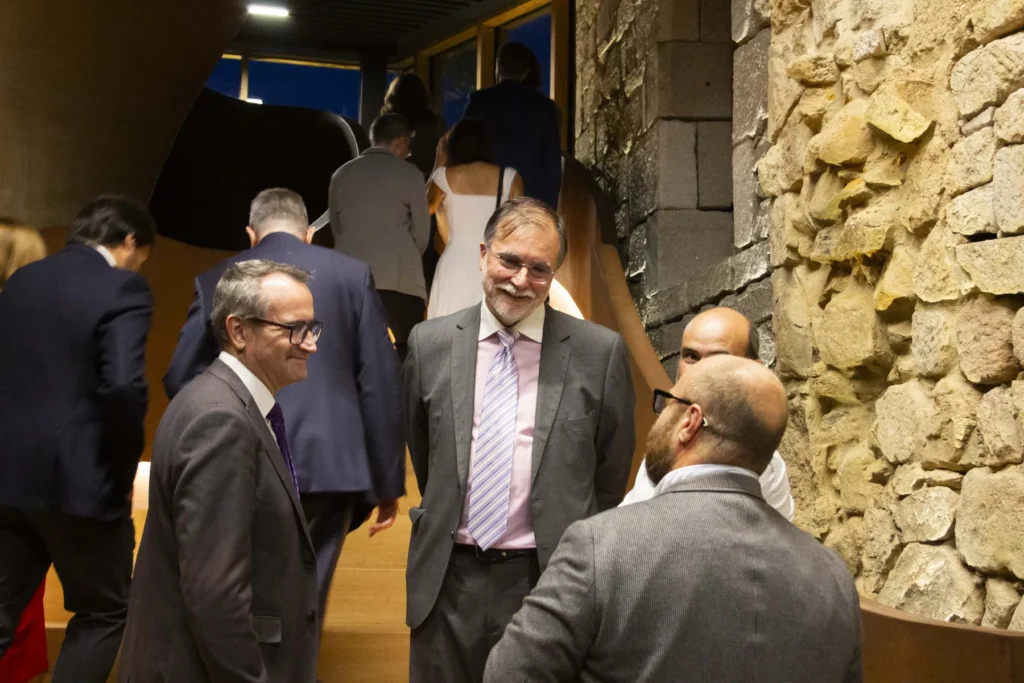 Catro homes conversan ao pé dunha escaleira de madeira mentres outros convidados soben ao fondo