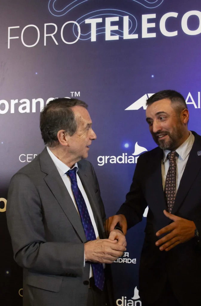 Dous homes conversan animadamente ante o panel de ForoTelecos, un deles xesticulando coas mans